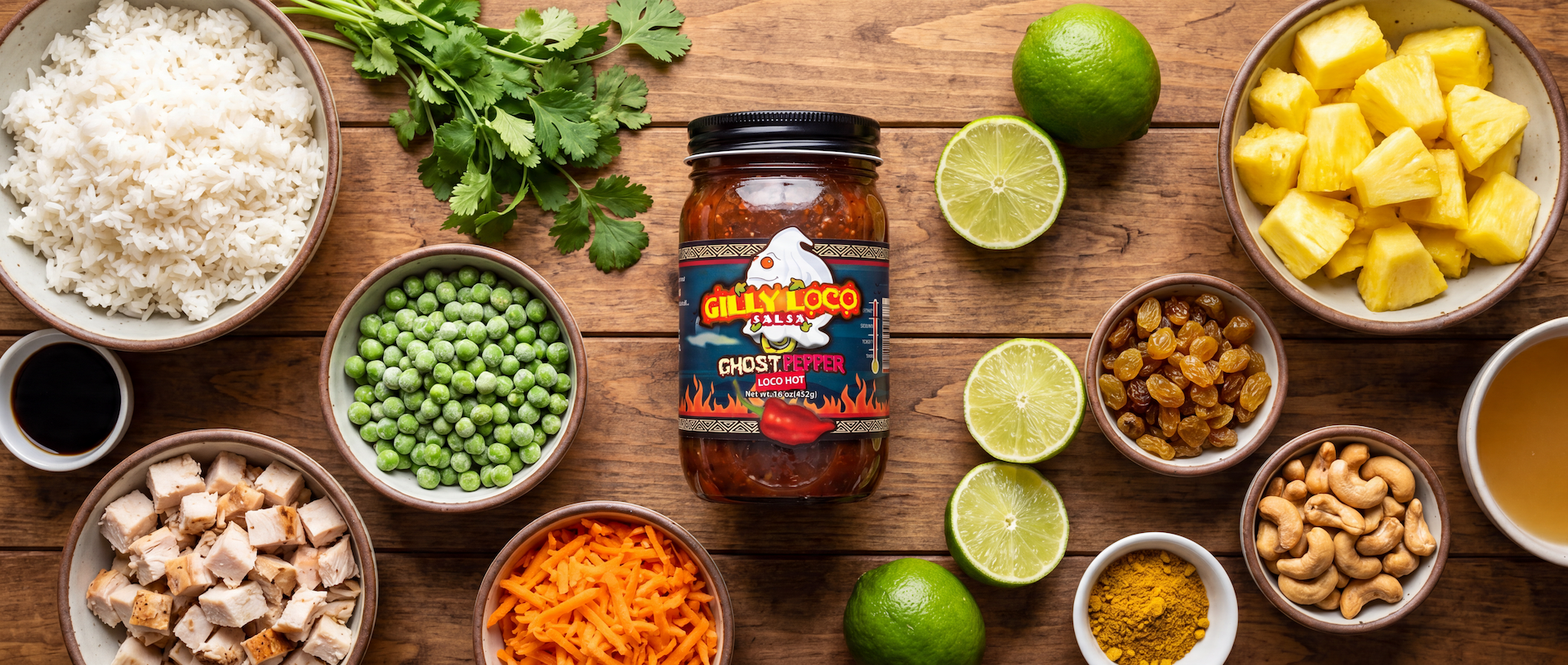 Ingredients for Gilly Loco Ghost Pepper Pineapple Fried Rice arranged on a rustic wood table with pineapple, jasmine rice, chicken, peas, carrots, raisins, cashews, cilantro, lime, soy sauce, curry powder, and Ghost Pepper Salsa.