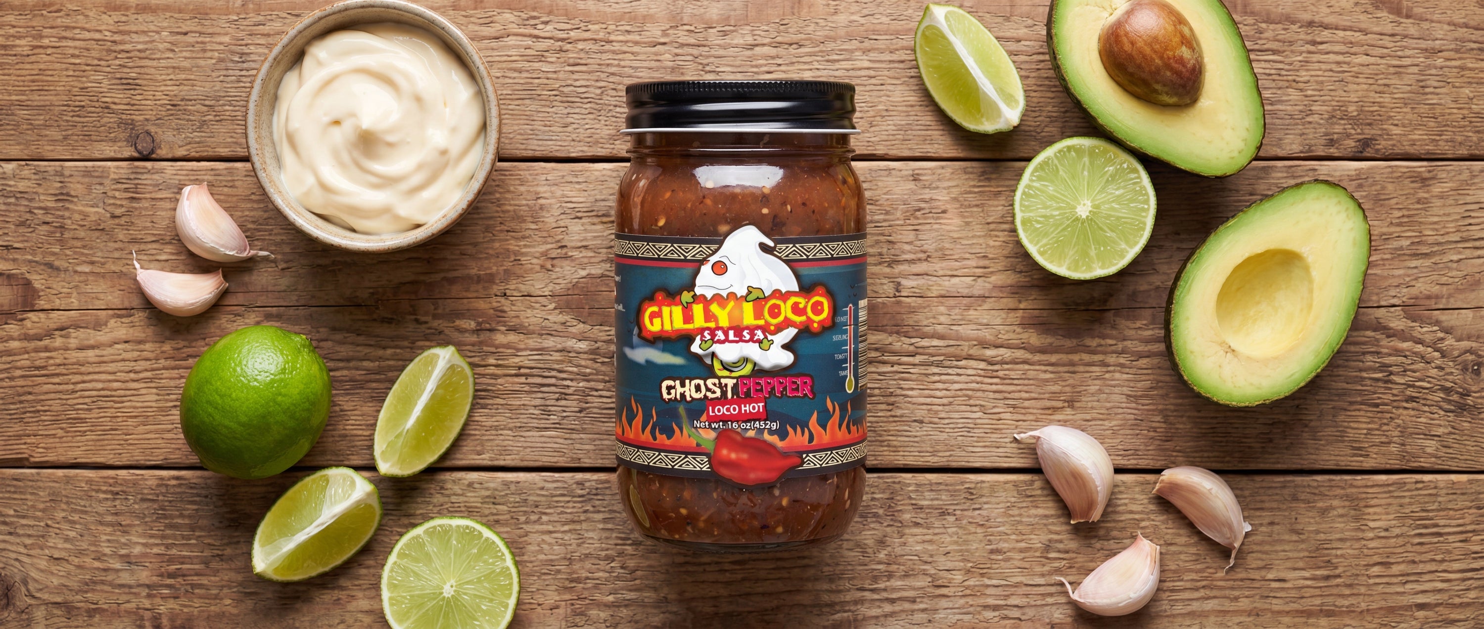 Gilly Loco Ghost Pepper Salsa jar surrounded by mayonnaise, garlic, lime, and avocado on a rustic wooden table for a burger sauce recipe.