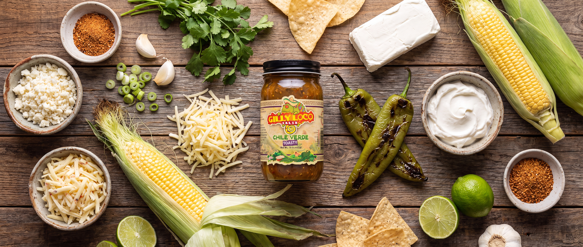 Ingredients for Hatch Green Chile Street Corn Dip including roasted Hatch green chile sauce, fresh corn, cotija cheese, Monterey Jack, cream cheese, sour cream, cilantro, lime, garlic, and Gilly Loco tortilla chips.