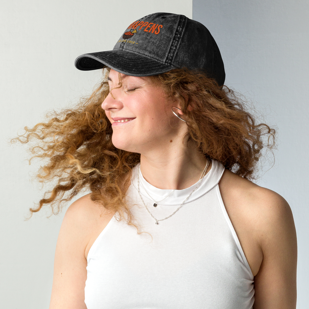 Woman wearing a black cap with text, smiling against a plain background
