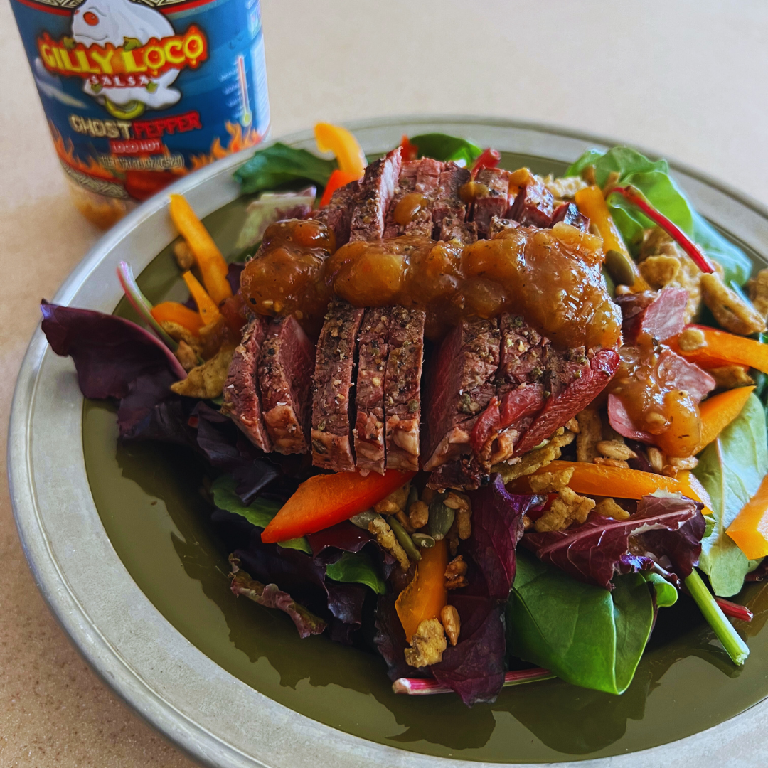 Image of a salad generously drizzled with Ghost Pepper Salsa Dressing made from Gilly Loco ghost pepper salsa. The dressing's vibrant red hue contrasts beautifully with the fresh greens, tomatoes, and cucumbers of the salad, highlighting the spicy and flavorful addition to a healthy dish.