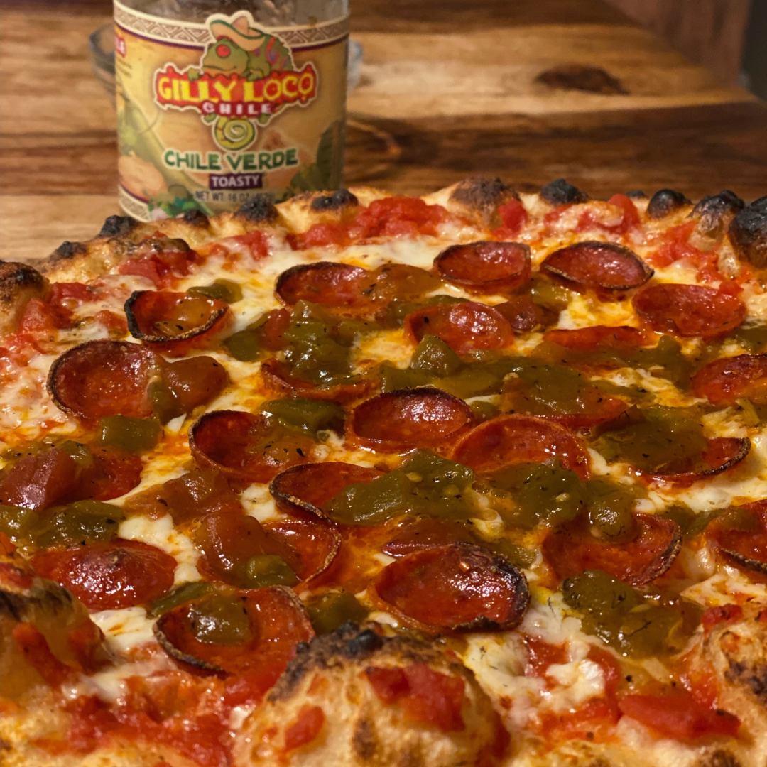 Photo of a pepperoni pizza generously topped with Hatch Green Chile sauce from Gilly Loco, adding a vibrant green hue to the classic dish. The chile sauce drizzles over the melted cheese and pepperoni slices, enhancing the pizza's appearance with a spicy and colorful twist.