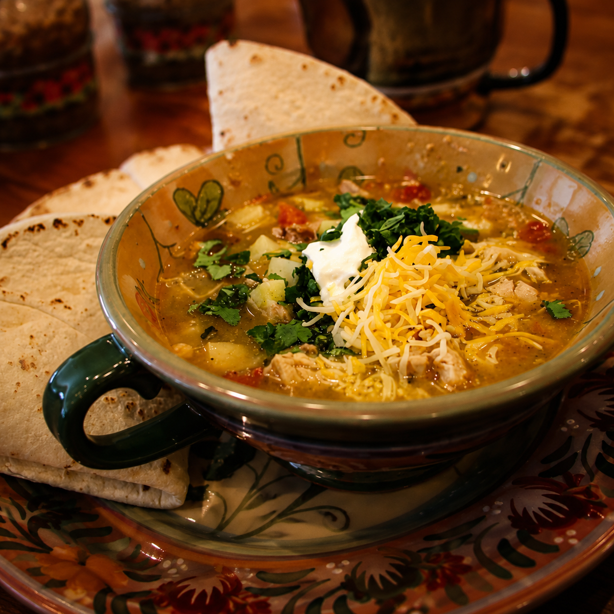 Square photo of Gilly Loco green chile stew topped with cheese, cilantro, and sour cream served with warm tortillas and authentic New Mexico flavor